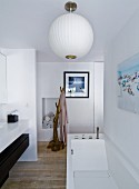 Moderne Badewanne unter weisser Kugellampe, seitlich Waschtisch, im Hintergrund naturbelassener Ast als Garderobe