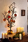 Gnarled fruit tree branch with Christmas tree baubles in glass vase; lit candles and wooden cow