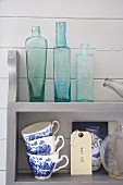 Collection of glass bottles and blue and white cups on wall-mounted shelves on wooden wall