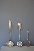 Antique silver ladles and slotted spoon leaning on wall