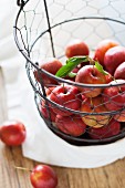 Red plums in a wire basket above a wooden table with a white cloth