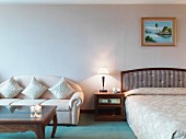 Doppelbett, Nachtkonsole & Sofa mit Dekokissen in Hotelzimmer