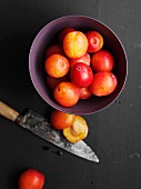 A bowl of plums next to a knife