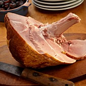 A partially sliced ham cut in a spiral on a cutting board with a knife