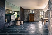 Sparsam möblierter Raum mit anthrazitfarbenen Bodenplatten in umgebautem Rustico; Natursteinwände im Kontrast mit verspiegelter Seitenwand
