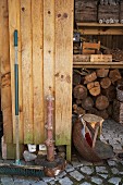 Alter Besen an Holzwand lehnend vor Holzlager und Kisten im Regal