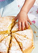 A child's hand reaching for a slice of Victoria Sponge Cake