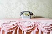 Stillleben mit grauem Vintage-Telefon auf rosafarbener Rüschentischdecke