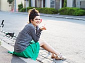 A young woman with a bicycle sitting on the pavement eating ice cream