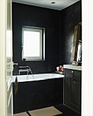 Blick durch offene Tür in schwarz getöntes Bad, seitlich teilweise sichtbarer Waschtisch neben Badewanne unter Fenster