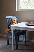 Soft toy sitting on kid's chair at table by window