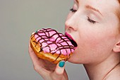 A young woman biting into a pink glazed doughnut, face cropped