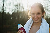 A portrait of a young female runner with a towel around her neck and a water bottle