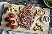 Grilled steak, mushrooms and tomatoes on a chopping board