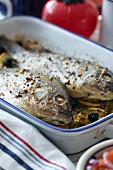 Two oven-baked fish on lemon slices in a roasting dish