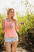 Junge blonde Frau spaziert im Park mit Wasserflasche und Smartphone