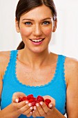 A young brunette woman holding raspberries in both hands