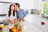 A man kissing a woman while preparing sandwiches in a kitchen