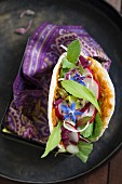 A pita bread filled with a mixed leaf salad, radishes and borage flowers