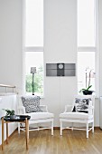 White armchairs and side table against wall with tall, narrow windows