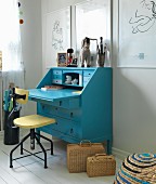 Vintage swivel chair at blue bureau below white-framed drawings on wall