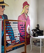 Vintage abacus next to antique telephone and typewriter on side table in front of pop art mural on wall