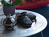 Mit Pailletten bestickte Lederpantoffeln und orientalische Teekanne auf marokkanischem Tabletttisch
