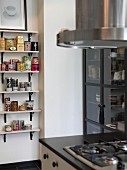 Gas cooker next to glass-fronted cabinet; colourful tea caddies and spice jars on wall-mounted shelves