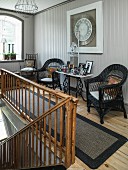Black wicker chairs ad framed photos on console table on landing with old wooden balustrade