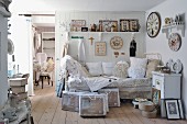 Daybed with lace cushions below collection of vintage clocks on white wooden wall and vintage-style ornaments on bracket shelf