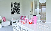 Pink crockery, thermos flask and lit tealights on white table in front of comfortable lounge area