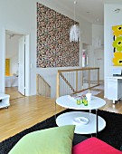 Lounge area with round, white side table, colourful cushions and large, multicoloured modern artwork above head of staircase