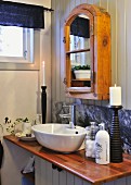 Rustic mirrored cabinet above washstand with varnished beach worksurface and stone splashback