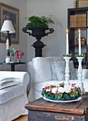 Wreath of flowers in front of lit candles in white, ceramic candlesticks on wooden trunk in corner of living room
