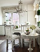 White-painted, Biedermeier-style side table in front of dining area below chandelier with glass pendants in country-house kitchen