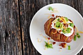 A Hasselback potato with a topping made from crème fraîche, spring onions, bacon and cheddar