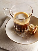 A macchiato in a glass cup on a saucer with biscotti