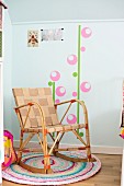 Schaukelstuhl mit Gurtbespannung auf buntem Häkelteppich und Wandtattoo im Kinderzimmer