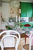 White Thonet chairs at table, lit candles in silver candlestick and bowl of fresh strawberries
