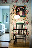 Green wooden chair and vintage standard lamp with pale lampshade against floral wallpaper next to open doorway