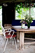 White, delicate metal chairs at rustic wooden table with vases of flowers on stone loggia floor