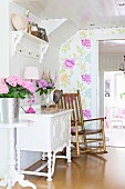 Wooden rocking chair next to flowers on white, ornate cabinet