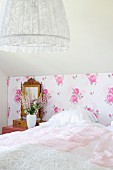 Bedroom with white bedspread on bed, nostalgic floral wallpaper and pendant lamp with lace lampshade