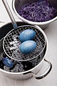 Eggs dyed using red cabbage on sieve spoon and pot of red cabbage