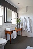 Rustic wooden table with countertop sink below windows in white tiled bathroom