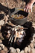 Vegetable stew in cooking pot suspended over campfire