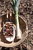 Skewers of grilled mushrooms on white dish and fresh leek on wooden stool outdoors