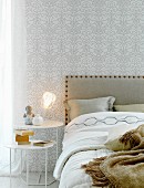 Beistelltisch neben Doppelbett, an Wand Tapete mit Ornamentmuster in Weiß und Silber