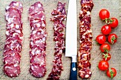 Salami- und Chorizoscheiben mit Messer und Kirschtomaten auf Schneidebrett