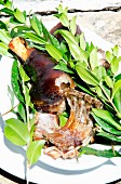 A piece of roast suckling pig on a plate with sprigs of fresh myrtle spurge (Sardinia)